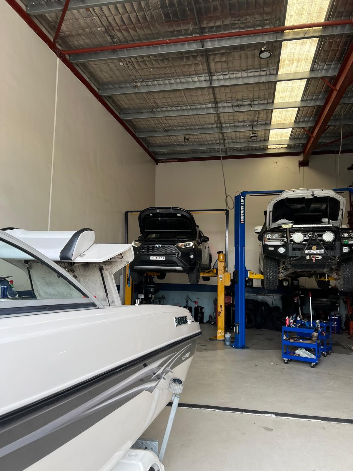 A boat on a trailer beside a Toyota RAV4 and Land Cruiser on hoists