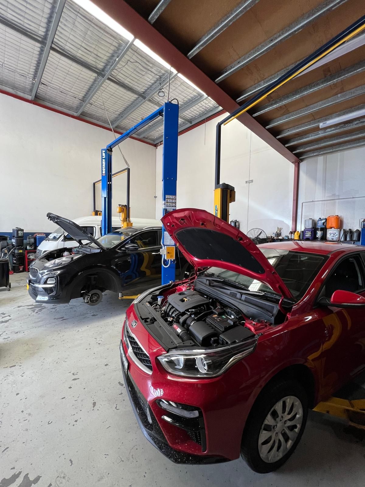 A Kia Sportage and Kia Cerato up on hoists with bonnets open